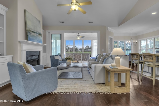 living room with vaulted ceiling, ceiling fan with notable chandelier, built in features, crown molding, and dark wood-type flooring