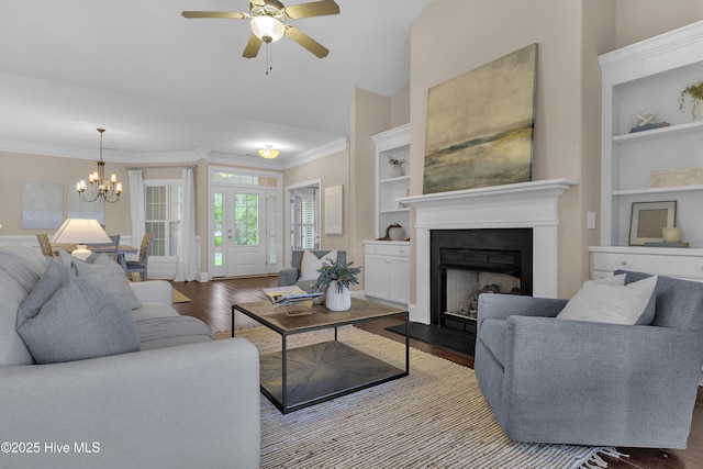 living room featuring hardwood / wood-style flooring, ornamental molding, ceiling fan with notable chandelier, and built in shelves