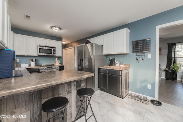 kitchen featuring stainless steel appliances, a kitchen breakfast bar, kitchen peninsula, and white cabinets