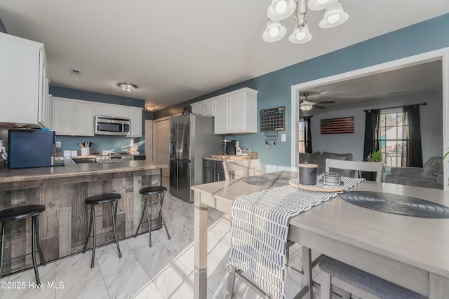 kitchen featuring ceiling fan with notable chandelier, appliances with stainless steel finishes, white cabinets, decorative light fixtures, and kitchen peninsula