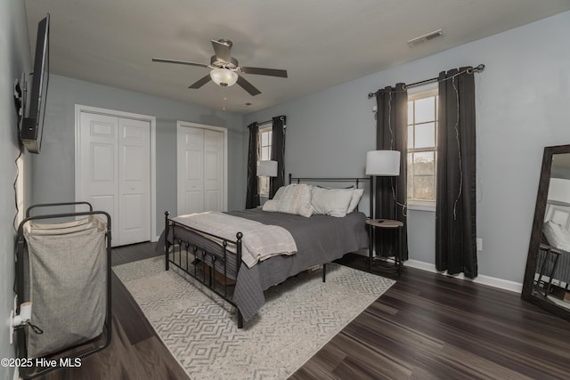 bedroom featuring multiple closets, dark hardwood / wood-style floors, and ceiling fan