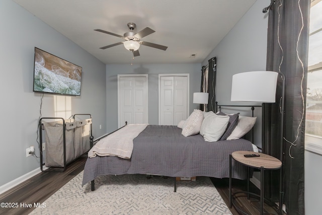 bedroom with dark wood-type flooring, ceiling fan, and two closets