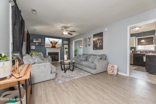 living room with ceiling fan, sink, and light wood-type flooring