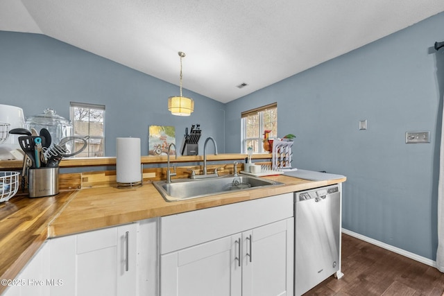 kitchen featuring decorative light fixtures, lofted ceiling, sink, wooden counters, and stainless steel dishwasher