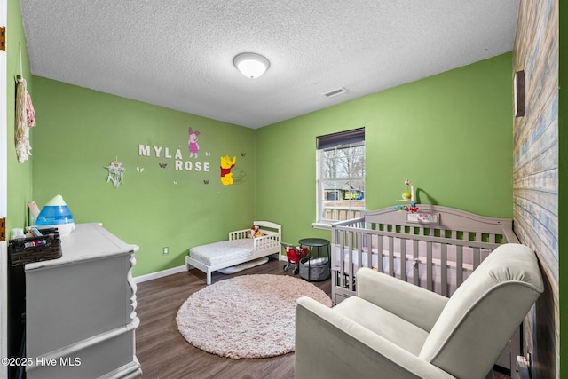 bedroom with hardwood / wood-style flooring, a nursery area, and a textured ceiling