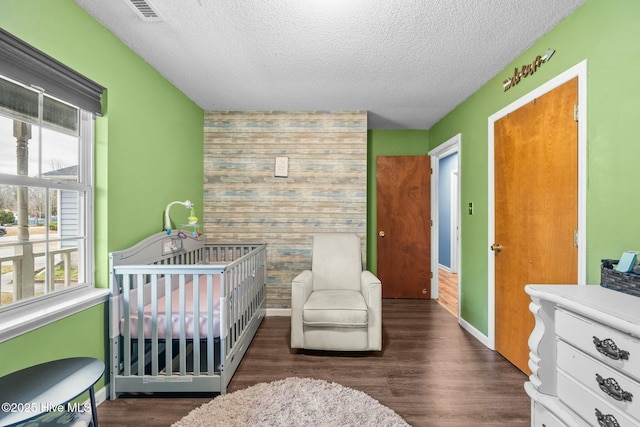 bedroom with a crib, dark hardwood / wood-style floors, and a textured ceiling