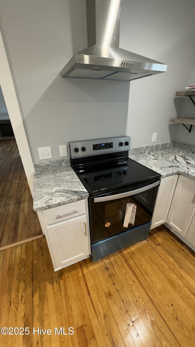 kitchen with electric stove, white cabinetry, light stone counters, wall chimney range hood, and light hardwood / wood-style flooring