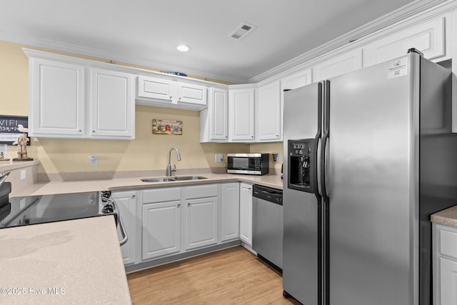 kitchen with appliances with stainless steel finishes, sink, white cabinets, ornamental molding, and light hardwood / wood-style floors