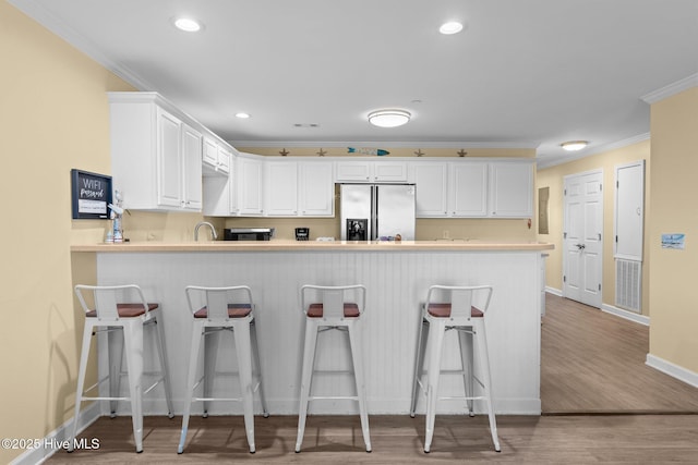 kitchen featuring appliances with stainless steel finishes, white cabinetry, ornamental molding, a kitchen bar, and kitchen peninsula