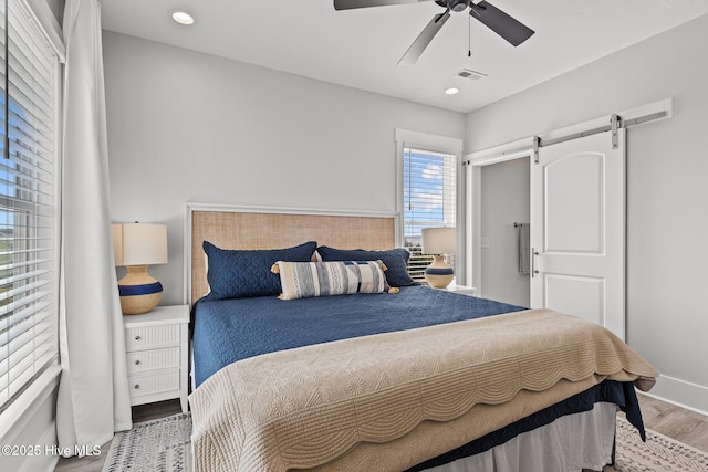 bedroom featuring hardwood / wood-style flooring, a barn door, and ceiling fan