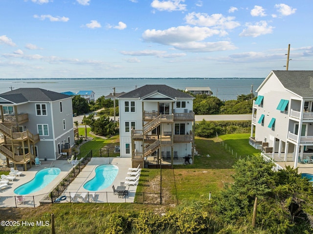 back of property featuring a balcony, a yard, a fenced in pool, a water view, and a patio area