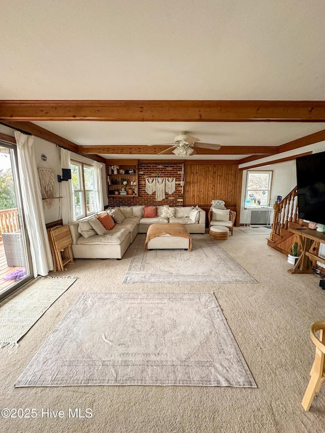 unfurnished living room featuring ceiling fan, carpet floors, beam ceiling, and wood walls