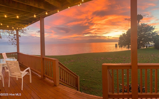 deck at dusk with a water view and a lawn