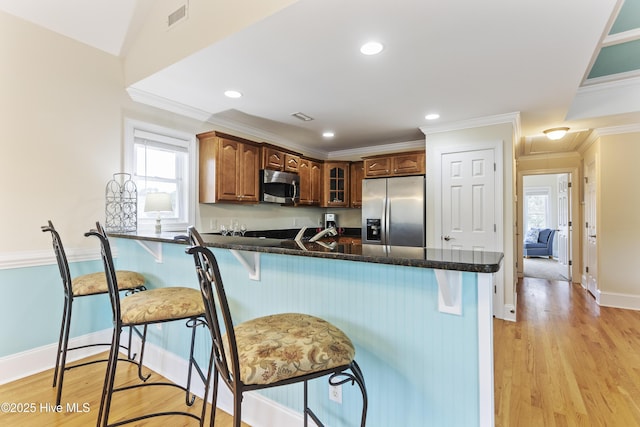 kitchen featuring light hardwood / wood-style flooring, ornamental molding, appliances with stainless steel finishes, a kitchen breakfast bar, and kitchen peninsula