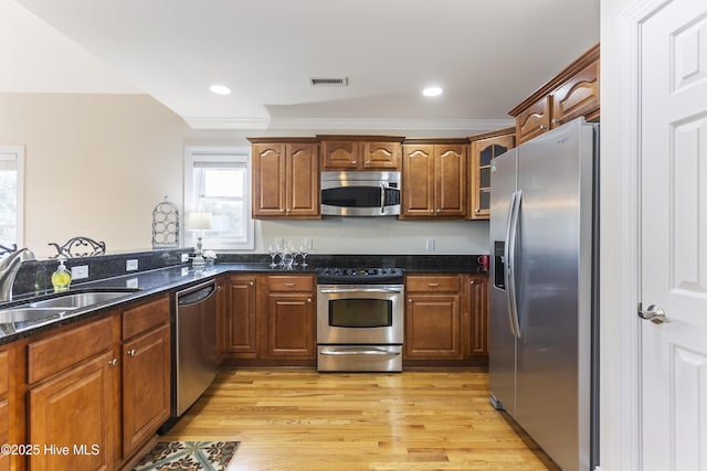 kitchen with sink, crown molding, light hardwood / wood-style flooring, stainless steel appliances, and dark stone counters