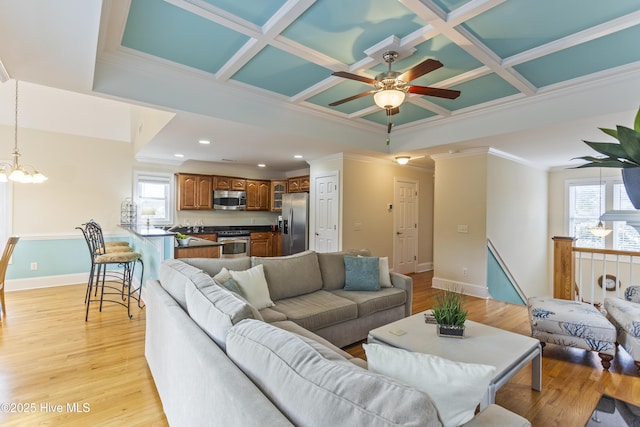 living room featuring coffered ceiling, crown molding, light hardwood / wood-style flooring, beamed ceiling, and ceiling fan with notable chandelier