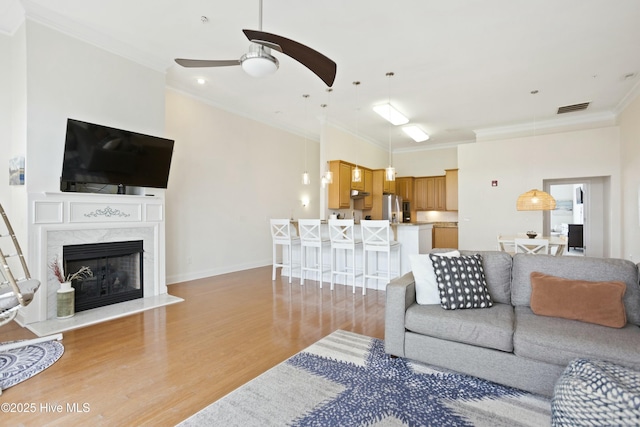 living room with crown molding, ceiling fan, a high end fireplace, and light hardwood / wood-style flooring