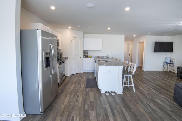 kitchen with sink, appliances with stainless steel finishes, white cabinetry, light stone counters, and a center island with sink