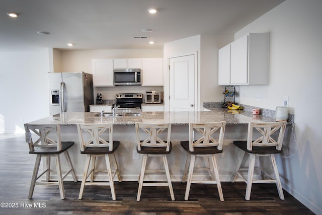 kitchen with a breakfast bar area, white cabinetry, light stone counters, dark hardwood / wood-style flooring, and stainless steel appliances