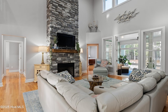 living room with light wood-style flooring, a high ceiling, baseboards, and a stone fireplace