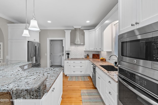 kitchen featuring a center island, stainless steel appliances, white cabinetry, a sink, and wall chimney exhaust hood