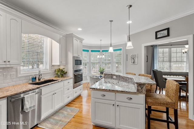 kitchen with a breakfast bar, decorative light fixtures, appliances with stainless steel finishes, white cabinets, and a sink