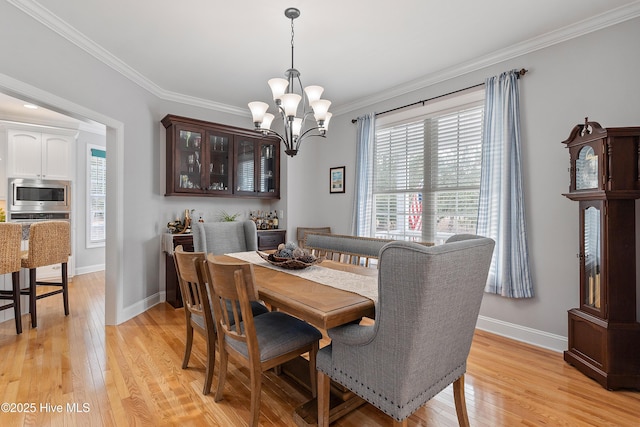 dining room with light wood-type flooring, a notable chandelier, baseboards, and crown molding