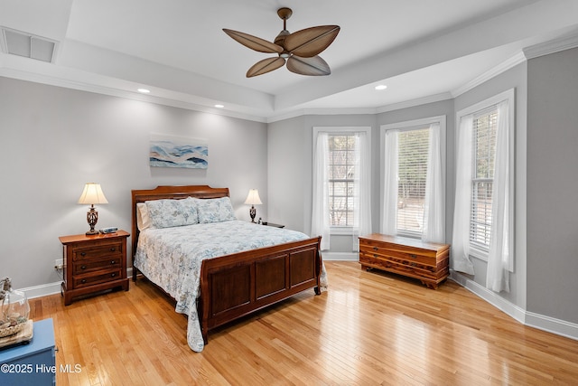 bedroom featuring light wood-type flooring, baseboards, visible vents, and a tray ceiling