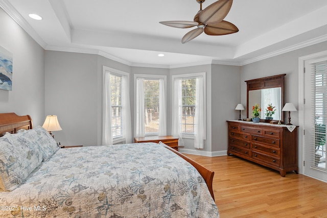 bedroom featuring baseboards, a raised ceiling, a ceiling fan, ornamental molding, and light wood-style floors