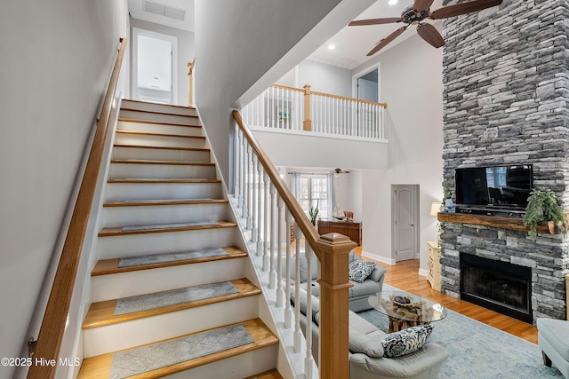 stairs with a fireplace, visible vents, a high ceiling, ceiling fan, and wood finished floors