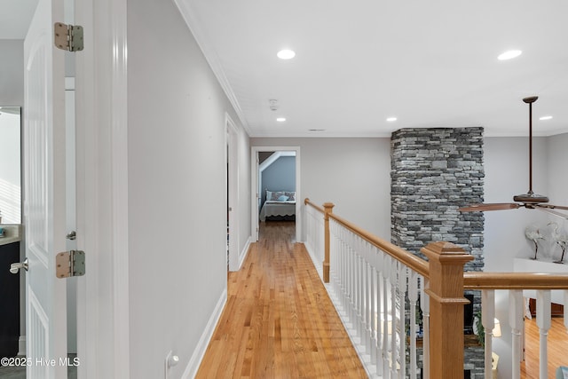 corridor featuring baseboards, ornamental molding, an upstairs landing, and light wood-style floors