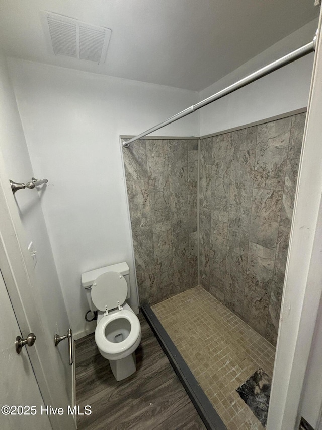 bathroom featuring hardwood / wood-style floors, toilet, and tiled shower