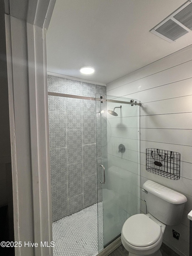 bathroom featuring a shower with shower door, wood walls, and toilet