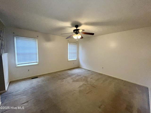 carpeted empty room featuring visible vents, a ceiling fan, and baseboards