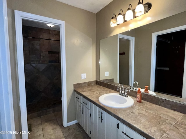 bathroom featuring vanity, tile patterned floors, baseboards, and tiled shower