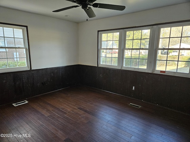 empty room featuring ceiling fan, dark hardwood / wood-style flooring, and wood walls