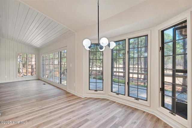 unfurnished dining area featuring vaulted ceiling, light wood-type flooring, baseboards, and an inviting chandelier