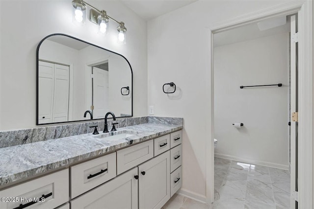 bathroom with toilet, marble finish floor, vanity, and baseboards