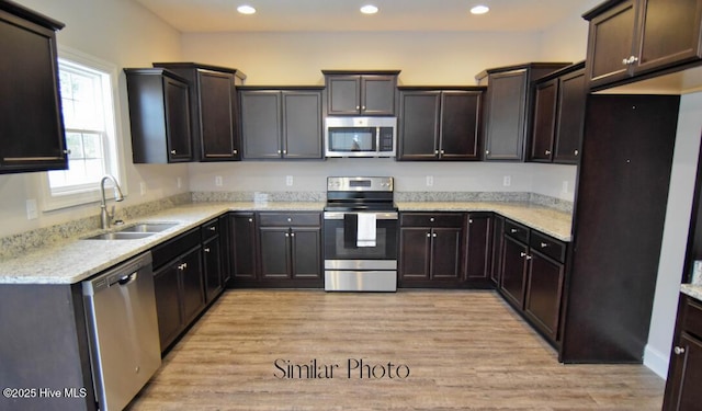 kitchen with stainless steel appliances, dark brown cabinets, sink, and light hardwood / wood-style floors