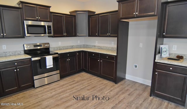 kitchen featuring light stone counters, light wood-type flooring, dark brown cabinetry, and appliances with stainless steel finishes