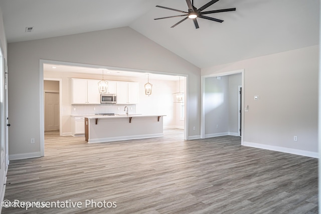 unfurnished living room featuring ceiling fan, lofted ceiling, and light wood-type flooring