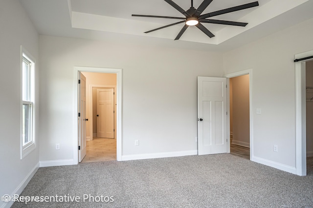 unfurnished bedroom featuring light carpet, ceiling fan, and a tray ceiling