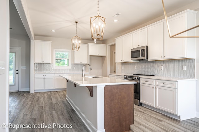 kitchen featuring sink, white cabinetry, stainless steel appliances, an island with sink, and decorative light fixtures