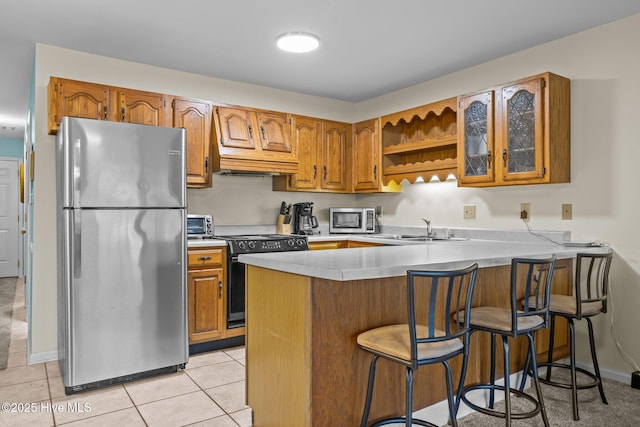 kitchen featuring a kitchen bar, sink, light tile patterned floors, kitchen peninsula, and stainless steel appliances