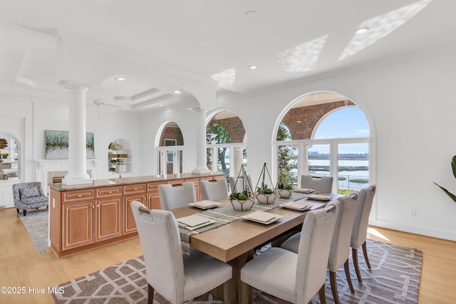 dining space featuring recessed lighting, a water view, ornate columns, and light wood-style floors