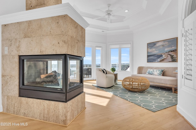 living area with a ceiling fan, a multi sided fireplace, crown molding, wood finished floors, and a high ceiling