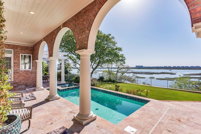 view of swimming pool with a lawn, fence, a pool with connected hot tub, a water view, and a patio area