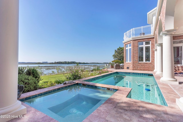 pool with a water view, a patio area, an in ground hot tub, and fence