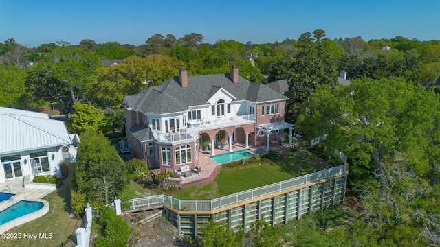 back of property featuring brick siding, an outdoor pool, a chimney, and a balcony