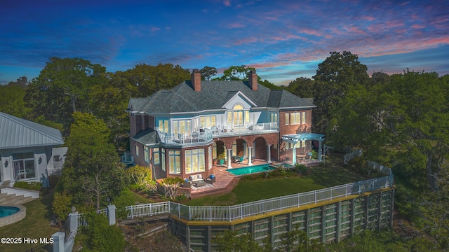 rear view of property with brick siding, a chimney, a fenced backyard, and a balcony